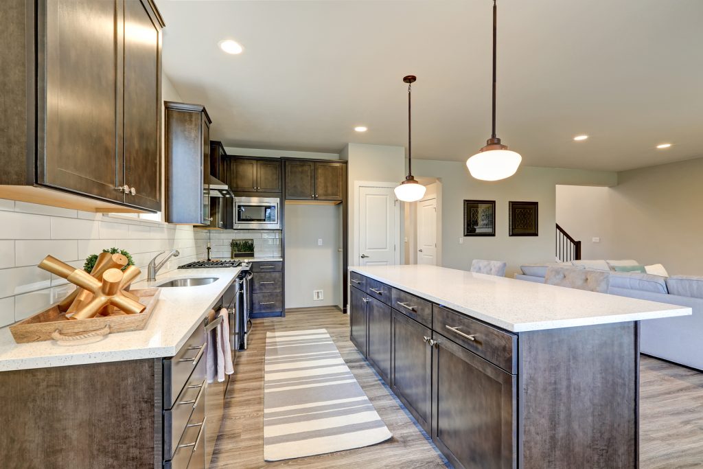 New kitchen boasts dark wood cabinets white backsplash subway tile and over sized island with white and grey quartz counter illuminated by pendant lights. Northwest USA